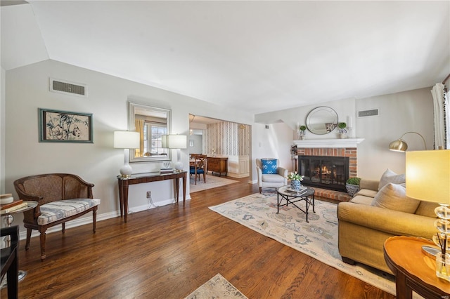 living room featuring visible vents, a brick fireplace, baseboards, and wood finished floors