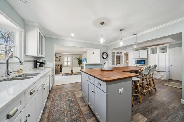 kitchen featuring wooden counters, a kitchen island, gray cabinetry, a breakfast bar area, and a sink