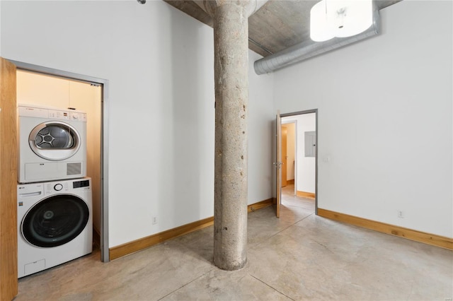 clothes washing area featuring a towering ceiling, stacked washing maching and dryer, baseboards, and laundry area