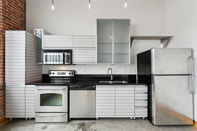 kitchen with dark countertops, appliances with stainless steel finishes, concrete flooring, gray cabinetry, and a sink