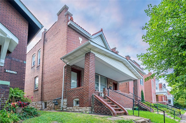 view of front facade featuring covered porch, stairway, a front lawn, and brick siding