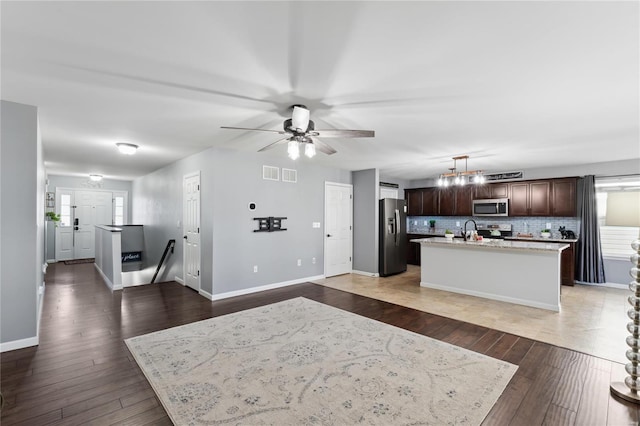 kitchen featuring light wood-style flooring, a kitchen island with sink, dark brown cabinetry, light countertops, and appliances with stainless steel finishes