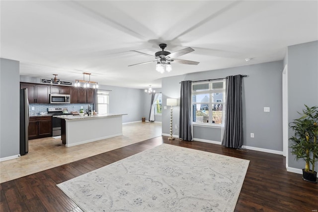 interior space featuring light wood-type flooring, baseboards, and ceiling fan with notable chandelier