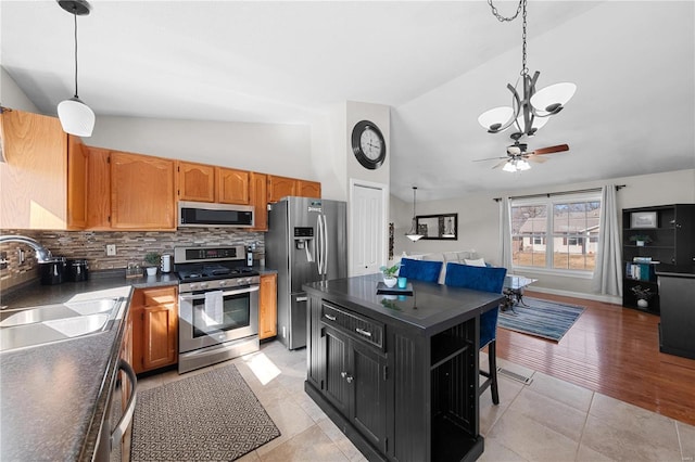 kitchen featuring appliances with stainless steel finishes, dark countertops, a sink, and hanging light fixtures