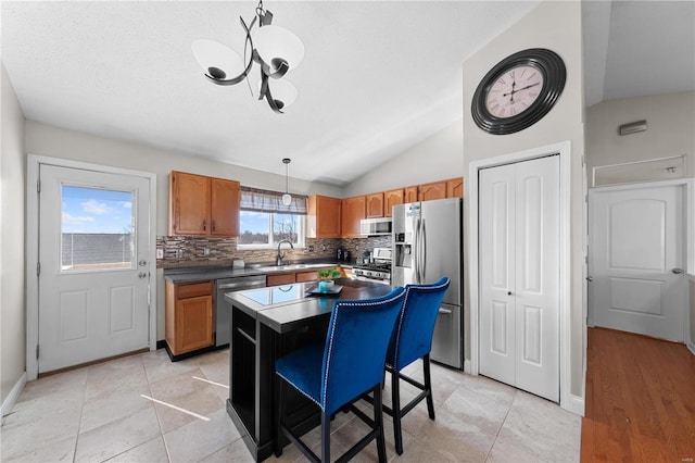 kitchen featuring decorative light fixtures, dark countertops, appliances with stainless steel finishes, a kitchen island, and a sink