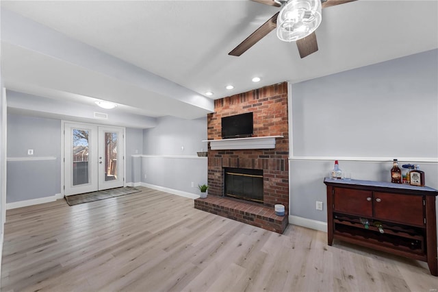 living area featuring a brick fireplace, baseboards, and light wood finished floors