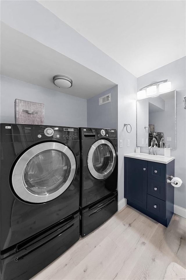 clothes washing area featuring baseboards, visible vents, light wood-style flooring, independent washer and dryer, and a sink