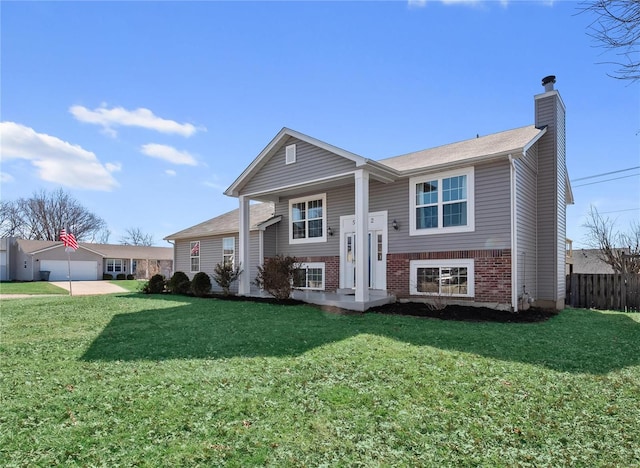 split foyer home featuring brick siding, a chimney, a front yard, and fence