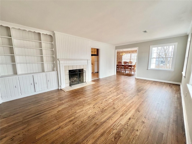 unfurnished living room featuring wood finished floors, baseboards, visible vents, a fireplace, and ornamental molding