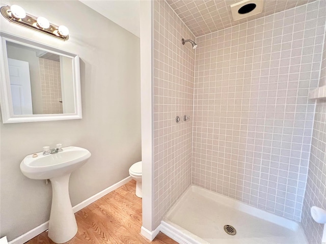 bathroom with toilet, wood finished floors, baseboards, and tiled shower