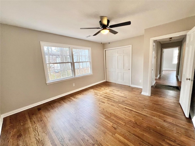 unfurnished bedroom featuring visible vents, ceiling fan, baseboards, wood finished floors, and a closet