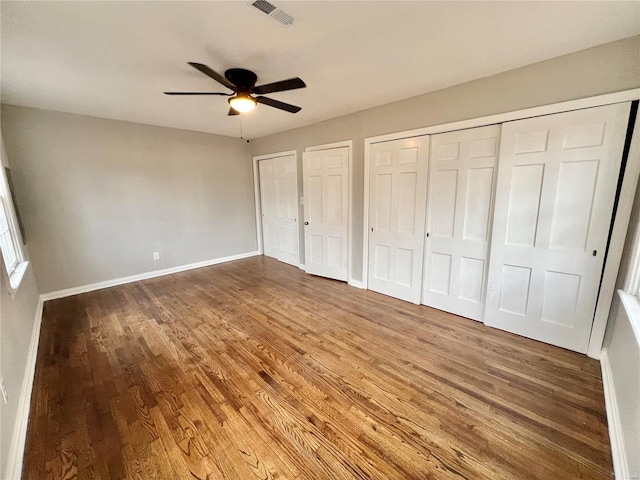 unfurnished bedroom featuring visible vents, two closets, baseboards, and wood finished floors