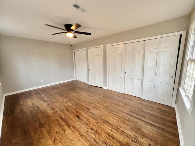 unfurnished bedroom featuring visible vents, two closets, baseboards, and wood finished floors