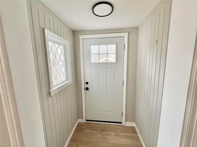 doorway to outside with baseboards, light wood-style floors, and wood walls