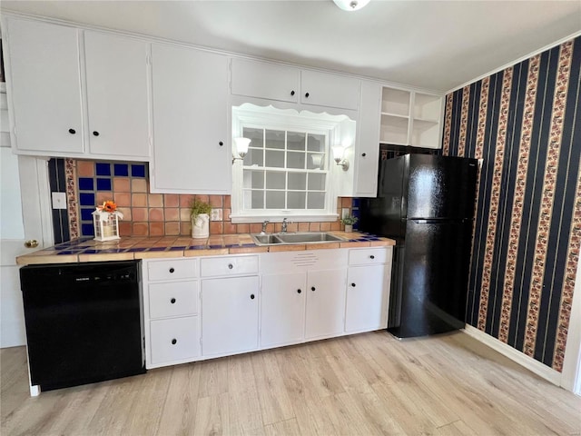 kitchen with black appliances, light wood-style flooring, a sink, tile countertops, and white cabinets