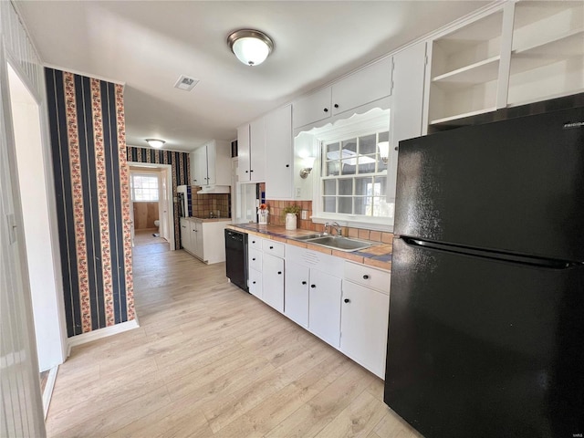 kitchen with light wood-style flooring, white cabinetry, black appliances, and a sink