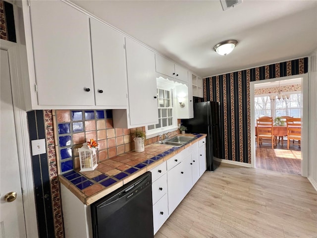 kitchen with wallpapered walls, tile counters, light wood-style flooring, white cabinets, and black appliances