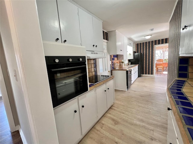 kitchen with wallpapered walls, black appliances, under cabinet range hood, white cabinetry, and light wood-type flooring