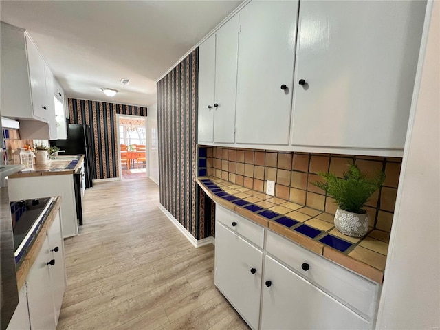 kitchen with tile countertops, wallpapered walls, light wood-style flooring, white cabinetry, and backsplash