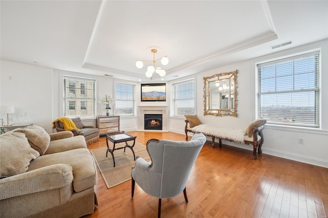 living room featuring light wood-style flooring, a raised ceiling, visible vents, and a healthy amount of sunlight