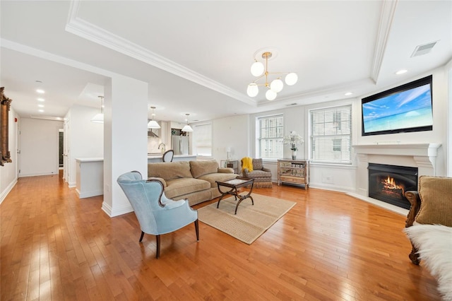 living area with a tray ceiling, crown molding, light wood finished floors, visible vents, and a lit fireplace