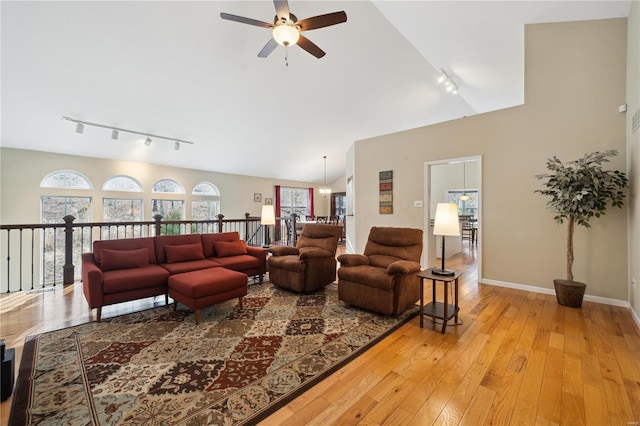 living area featuring rail lighting, light wood-style floors, a ceiling fan, vaulted ceiling, and baseboards