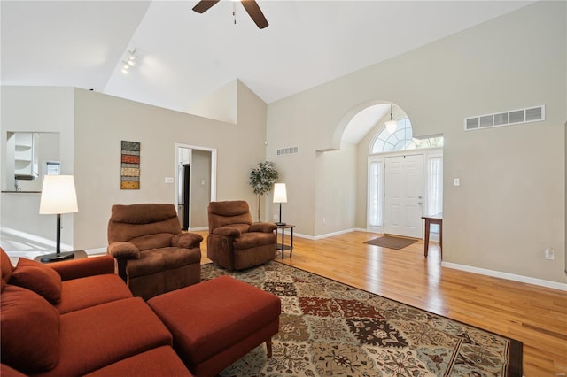 living area with high vaulted ceiling, baseboards, visible vents, and wood finished floors