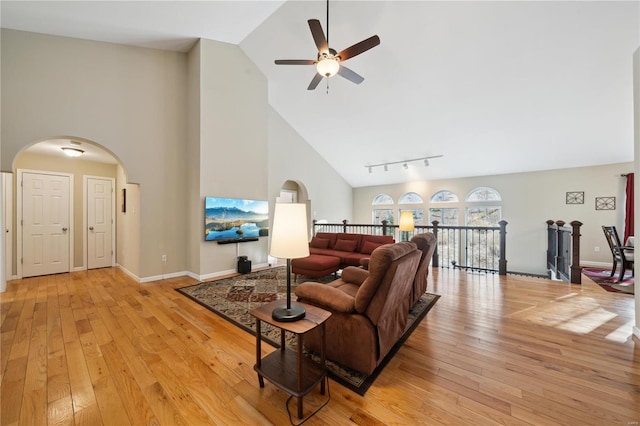 living room featuring high vaulted ceiling, light wood-style flooring, arched walkways, and baseboards