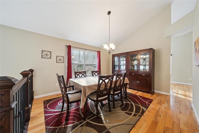 dining area with light wood-style floors, high vaulted ceiling, baseboards, and an inviting chandelier