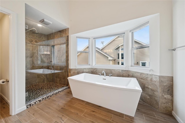 bathroom with wood finish floors, a soaking tub, a shower stall, and tile walls