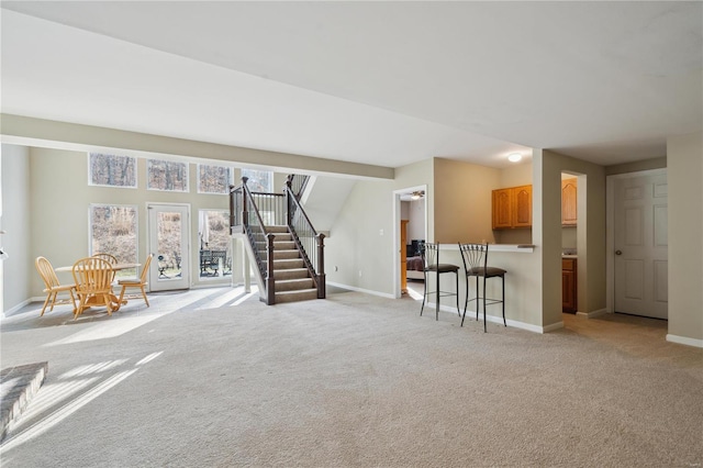 unfurnished living room featuring baseboards, stairway, and light colored carpet