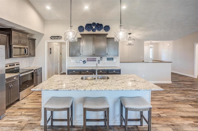 kitchen featuring a kitchen island with sink, pendant lighting, stainless steel appliances, and a sink