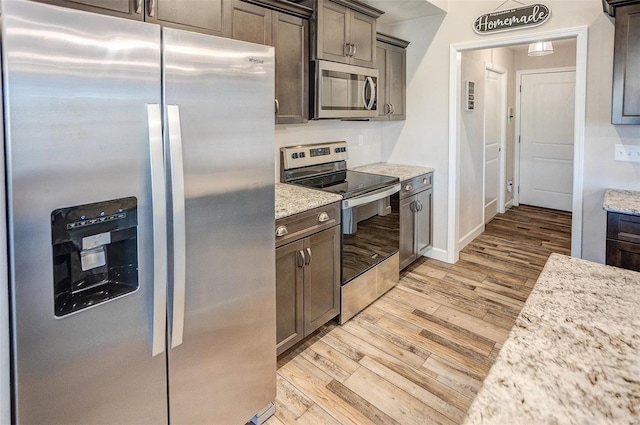 kitchen with appliances with stainless steel finishes, light wood-type flooring, dark brown cabinetry, and light stone counters