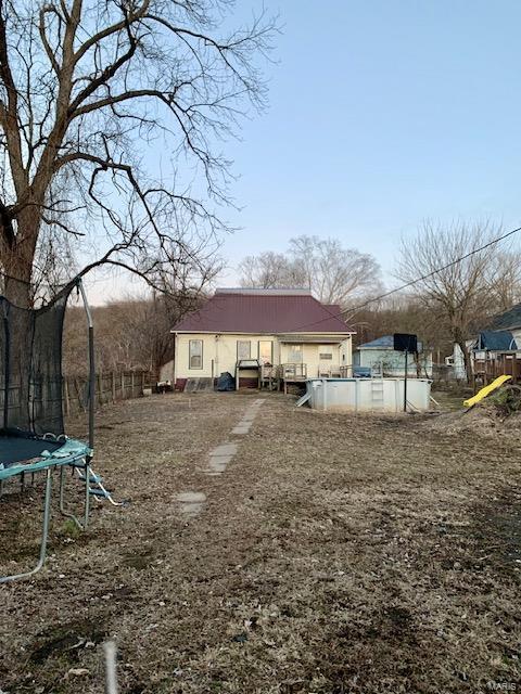 rear view of property featuring a trampoline and a pool