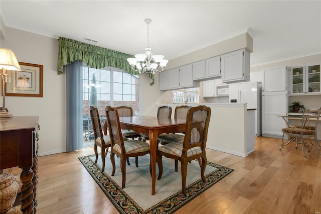 dining room with baseboards, visible vents, ornamental molding, light wood-type flooring, and a chandelier