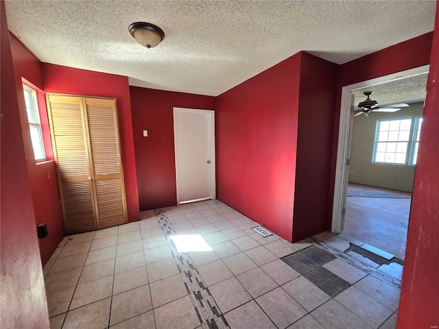 empty room with light tile patterned floors, ceiling fan, visible vents, and a textured ceiling