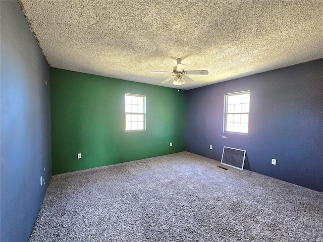 carpeted spare room featuring ceiling fan, a textured ceiling, visible vents, and a wealth of natural light