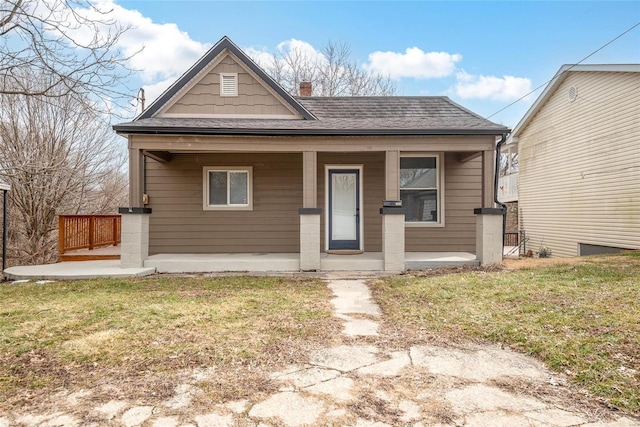 bungalow featuring a porch, a front yard, roof with shingles, and a chimney