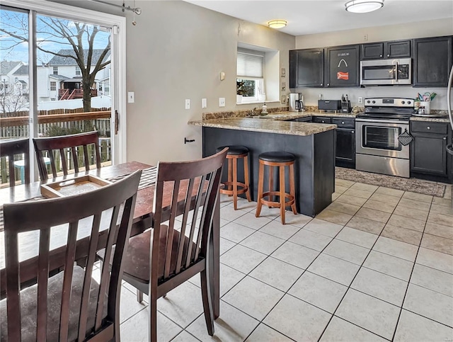 kitchen with light tile patterned floors, a peninsula, appliances with stainless steel finishes, and a healthy amount of sunlight