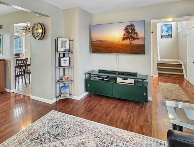 living room featuring baseboards, visible vents, a ceiling fan, stairway, and wood finished floors