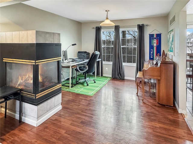 office space with a multi sided fireplace, wood finished floors, visible vents, and baseboards