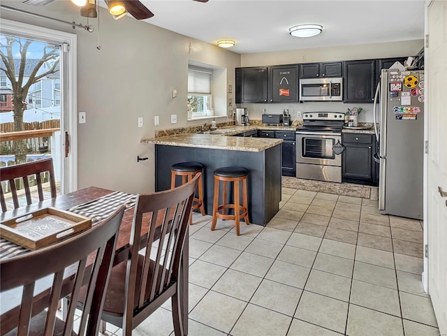 kitchen with a breakfast bar area, a peninsula, stainless steel appliances, a sink, and light tile patterned flooring