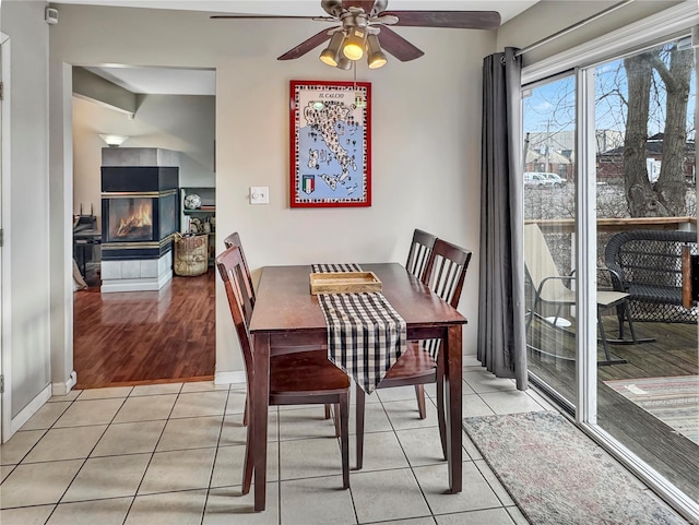 dining space featuring light tile patterned flooring, a tile fireplace, a ceiling fan, and baseboards