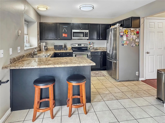 kitchen featuring light tile patterned floors, appliances with stainless steel finishes, a sink, a peninsula, and a kitchen breakfast bar