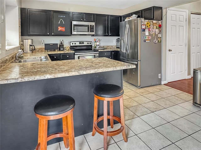 kitchen with appliances with stainless steel finishes, a sink, a peninsula, and light tile patterned floors