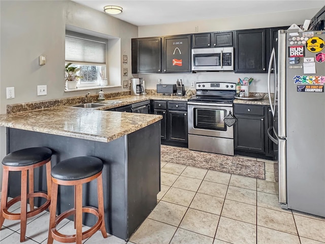 kitchen featuring light tile patterned floors, appliances with stainless steel finishes, a sink, a peninsula, and a kitchen bar