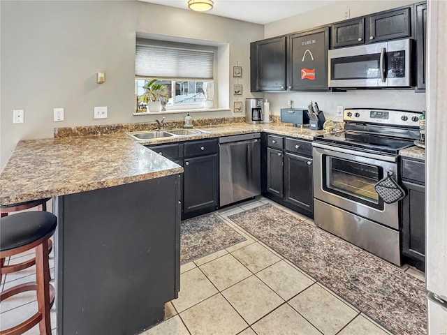 kitchen featuring light tile patterned flooring, stainless steel appliances, a peninsula, a sink, and a kitchen bar