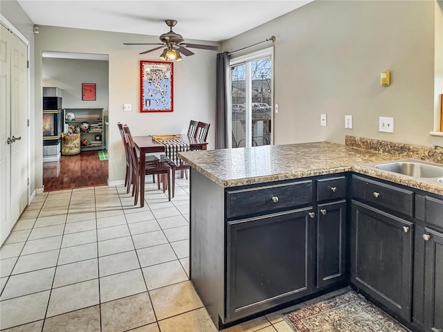 kitchen featuring baseboards, ceiling fan, a peninsula, a sink, and light tile patterned flooring