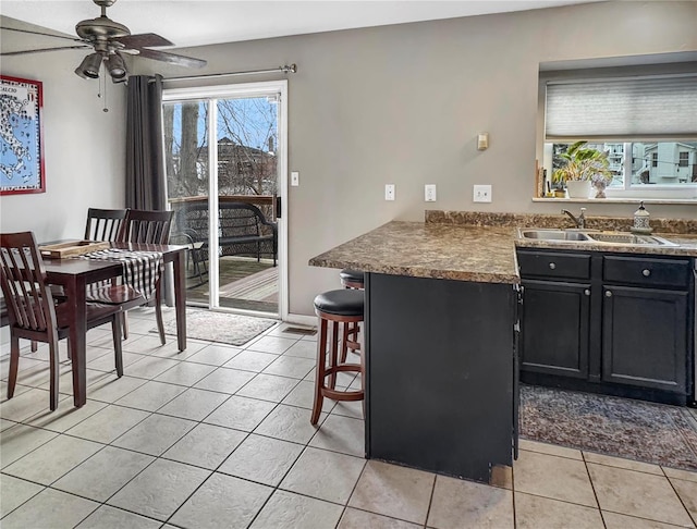 kitchen featuring light tile patterned floors, a sink, ceiling fan, dark cabinets, and a peninsula