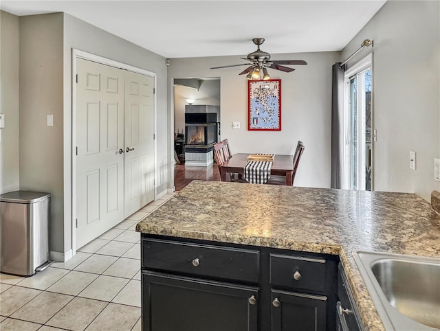 kitchen with light tile patterned floors, a tile fireplace, dark cabinets, a peninsula, and a ceiling fan